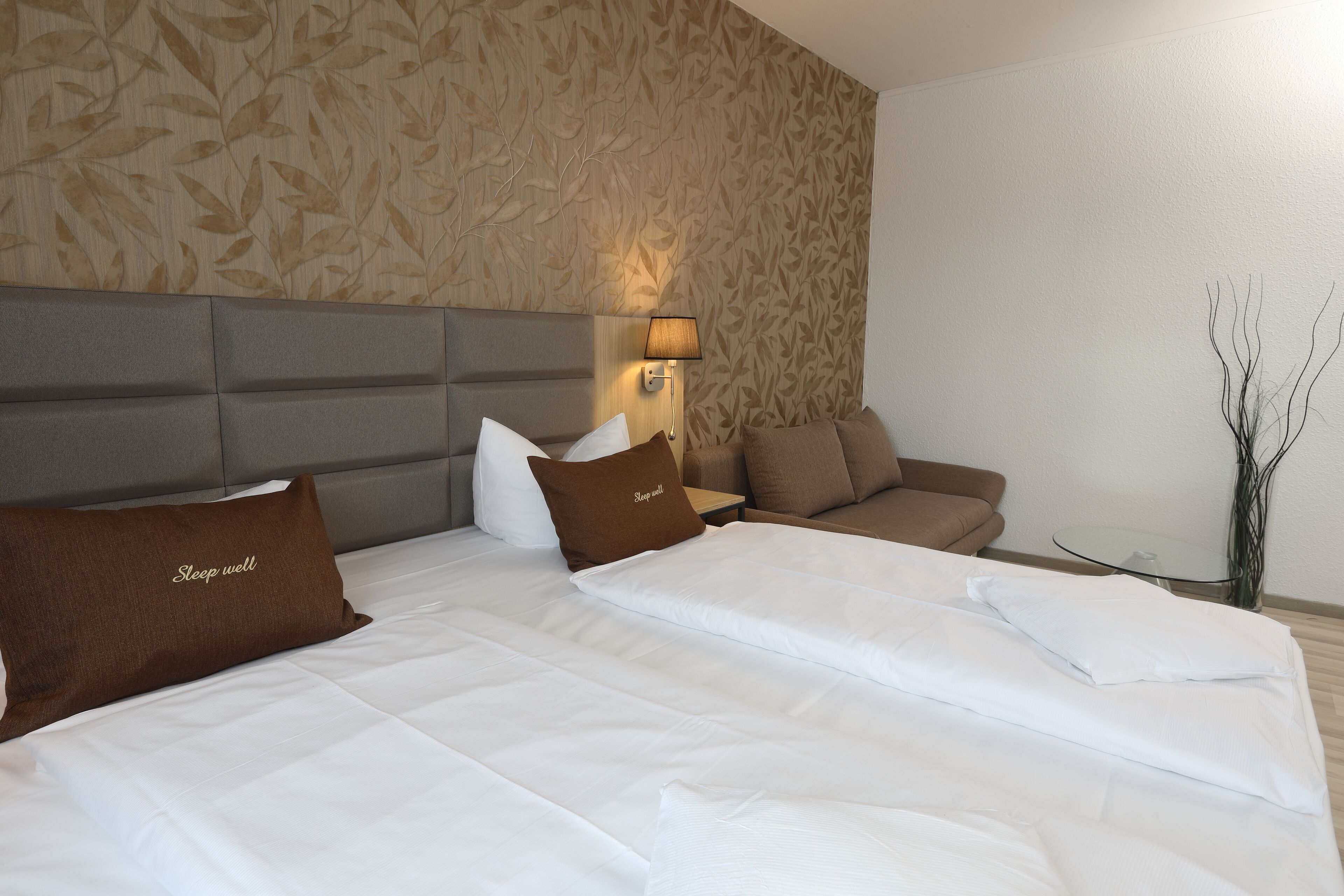 A hotel room with a large bed, a sofa, a small table, and a wall with a leaf pattern.