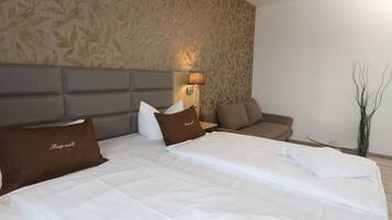 A hotel room with a large bed, a sofa, a small table, and a wall with a leaf pattern.