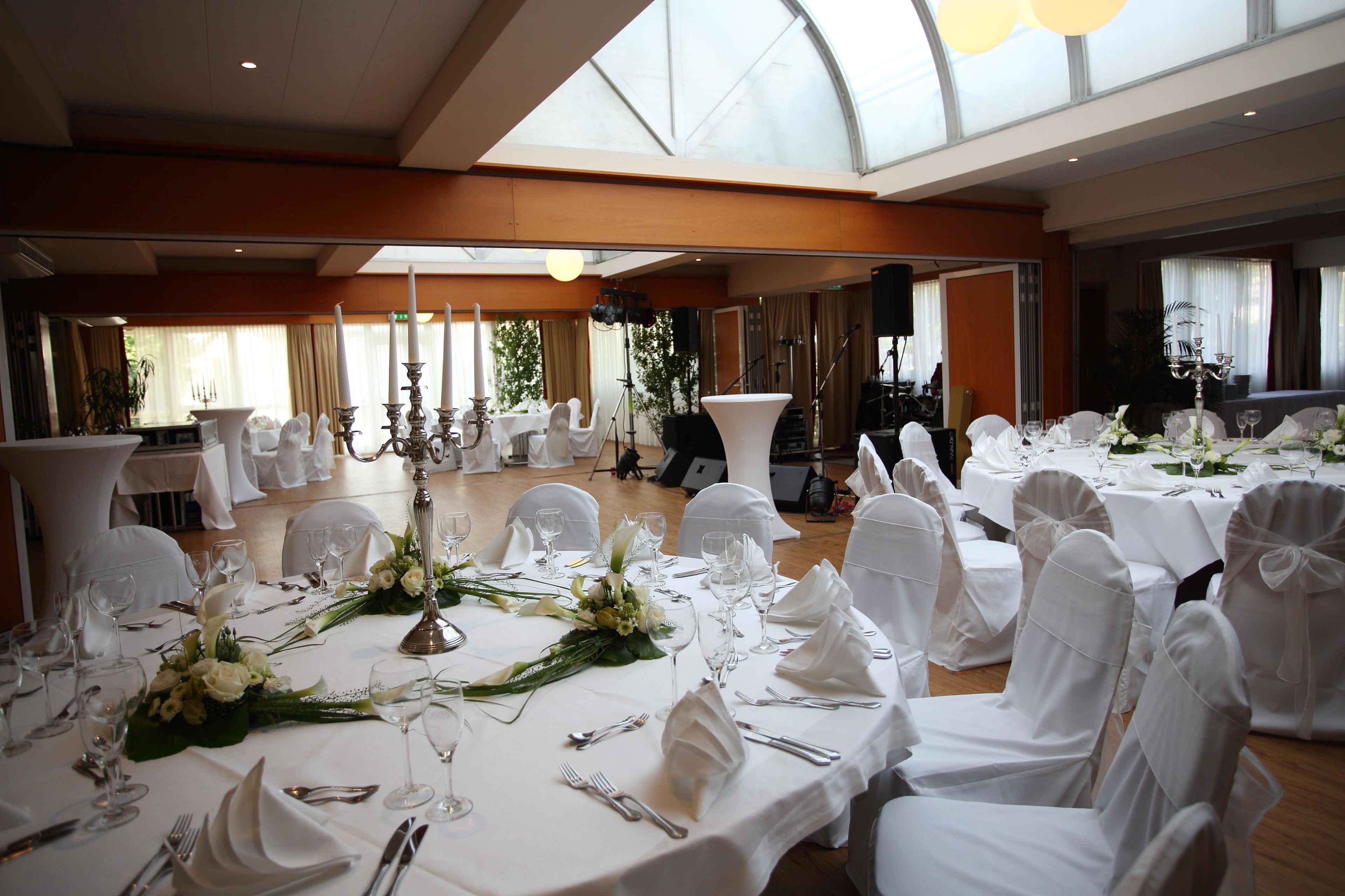 Un salón de banquetes con mesas redondas dispuestas para un evento formal, con manteles blancos, cristalería y centros de mesa florales.