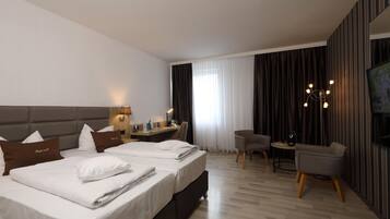 A hotel room with two beds, a desk, a chair, a TV, and a large window with curtains.