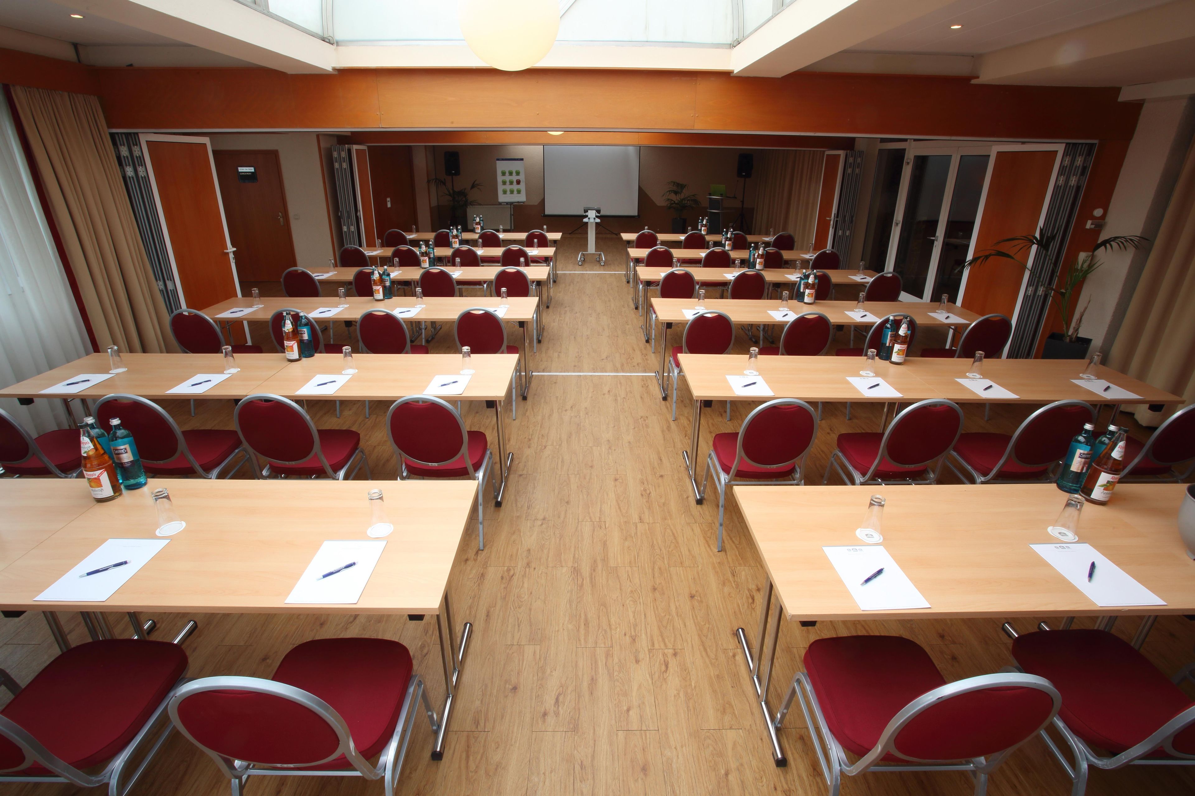 Un salón de conferencias con varias mesas y sillas, equipado con botellas de agua y bolígrafos.
