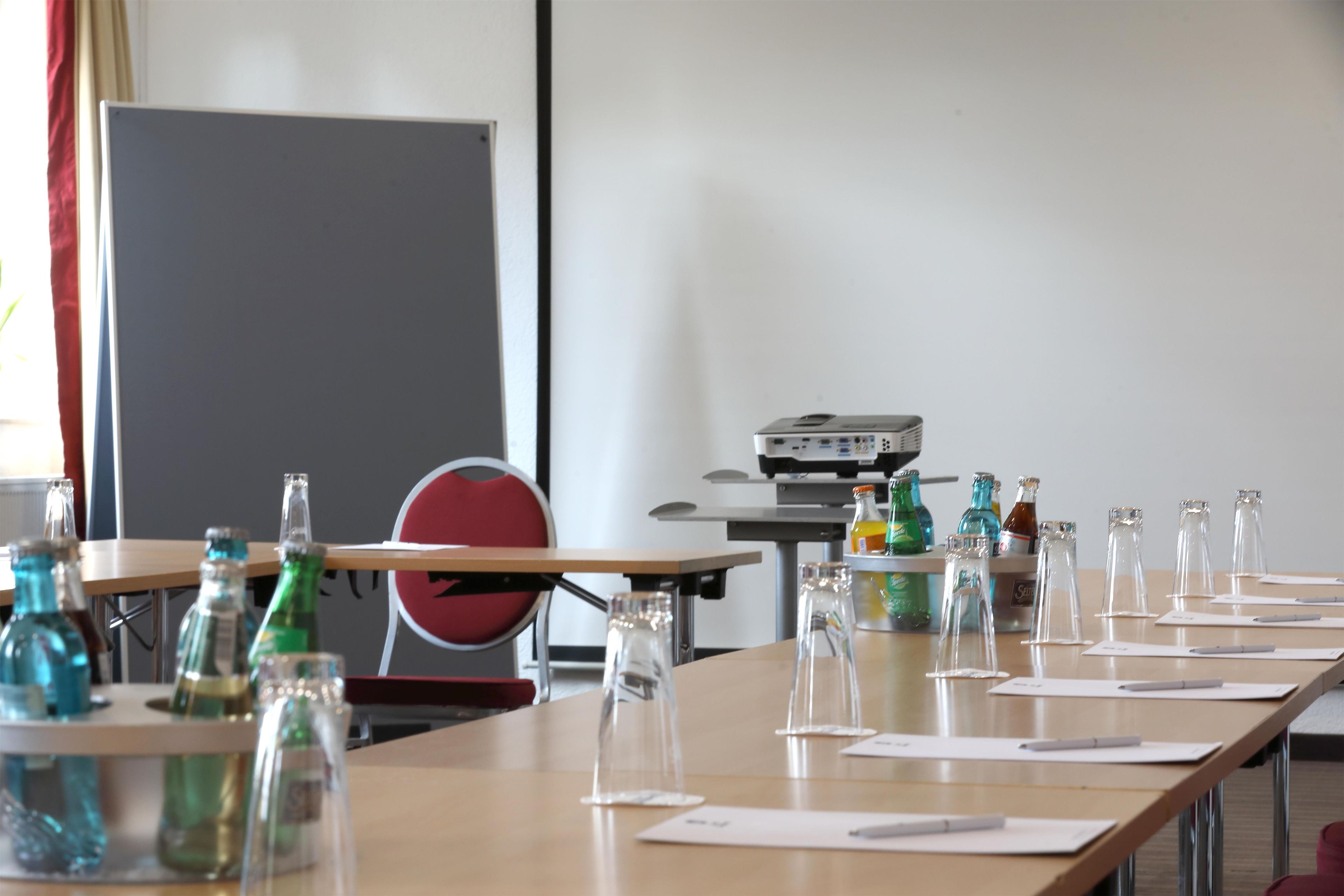A conference room with a long table, chairs, a projector, and various glass bottles and bottles.