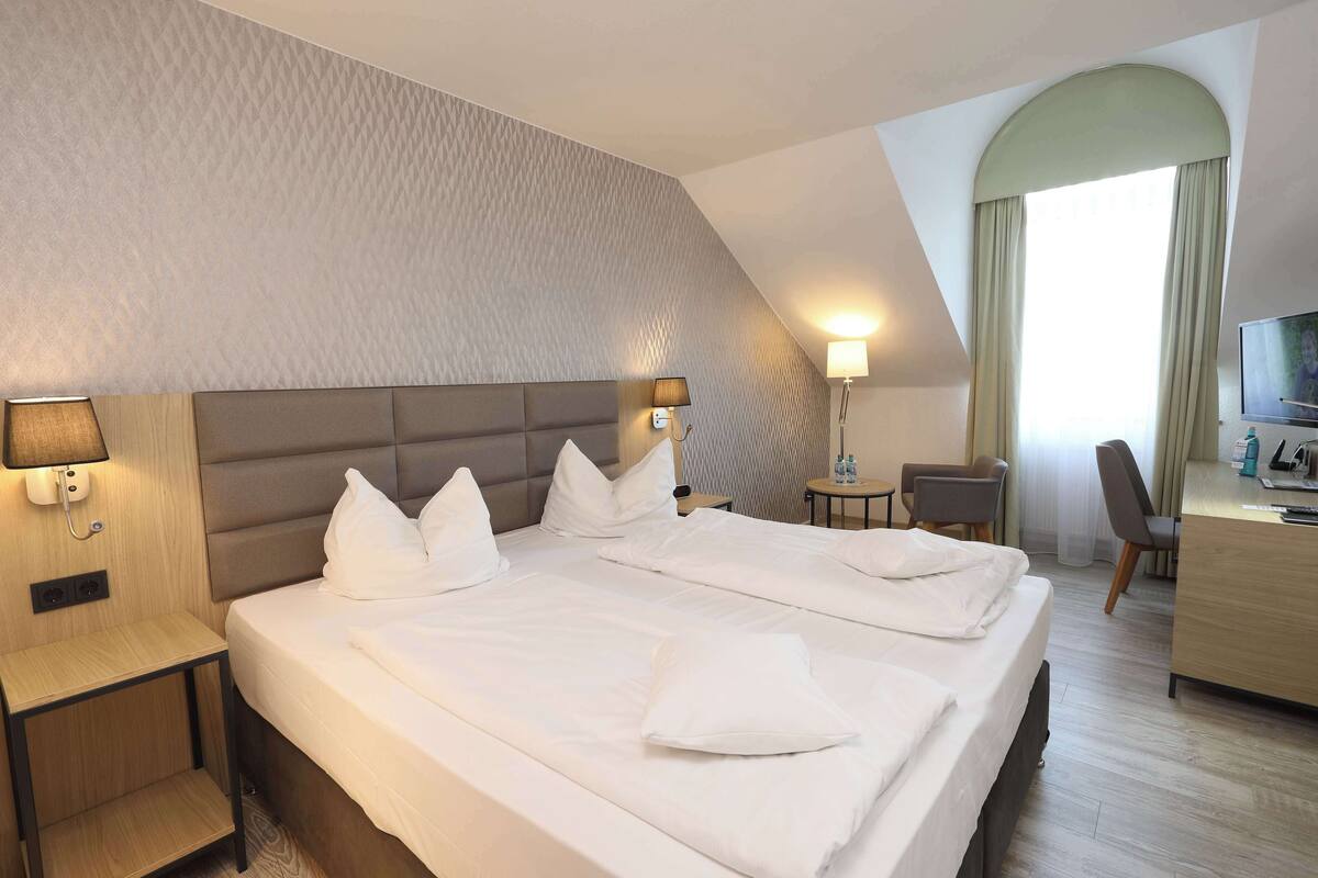 A hotel room with a large bed, two bedside tables, a desk, a chair, and a TV.