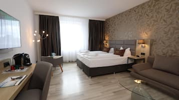 Ein Hotelzimmer mit einem Bett, einem Schreibtisch mit Kaffeemaschine, einer Sitzecke, einem Fernseher und einem Fenster mit Vorhängen.