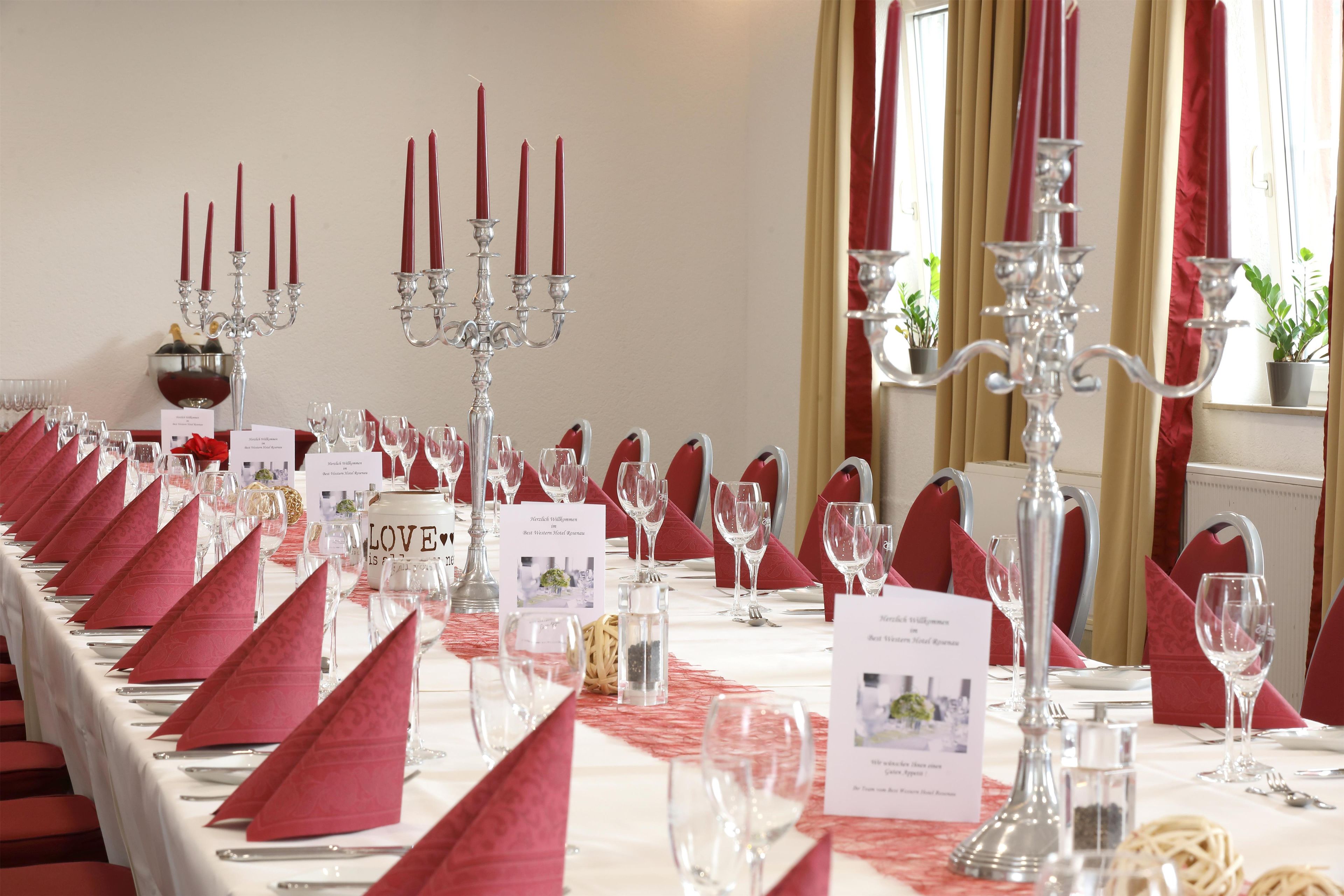 Een feesttafel gedekt met rode servetten, wijnglazen en een kandelaar.