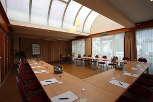 A conference room with a long table, red chairs, and a large window with curtains.