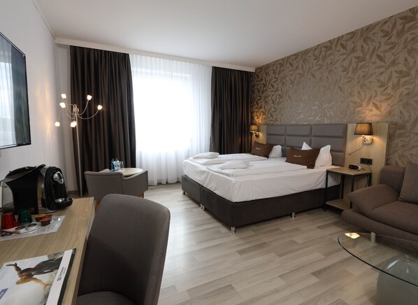 A hotel room with a large bed, a desk with a coffee machine, a sofa, and a glass coffee table. - Best Western Hotel Rosenau (Bad Nauheim)
