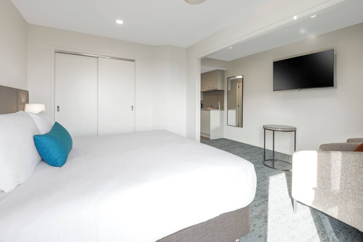 A hotel room with a large bed, a flat-screen TV, a small round table, and a seating area.