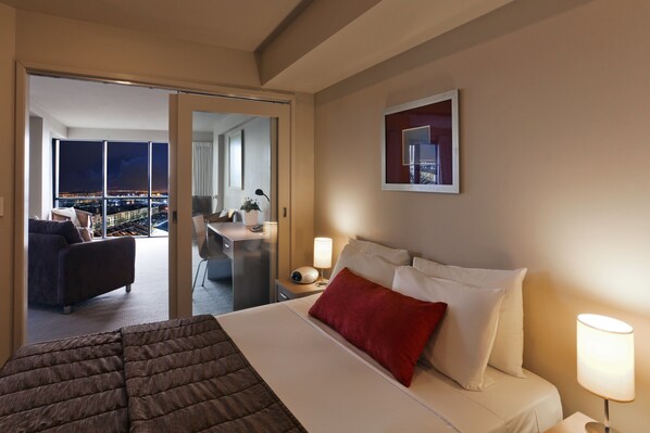 Une chambre d’hôtel avec un lit, un bureau, une chaise et une vue sur la ville la nuit.