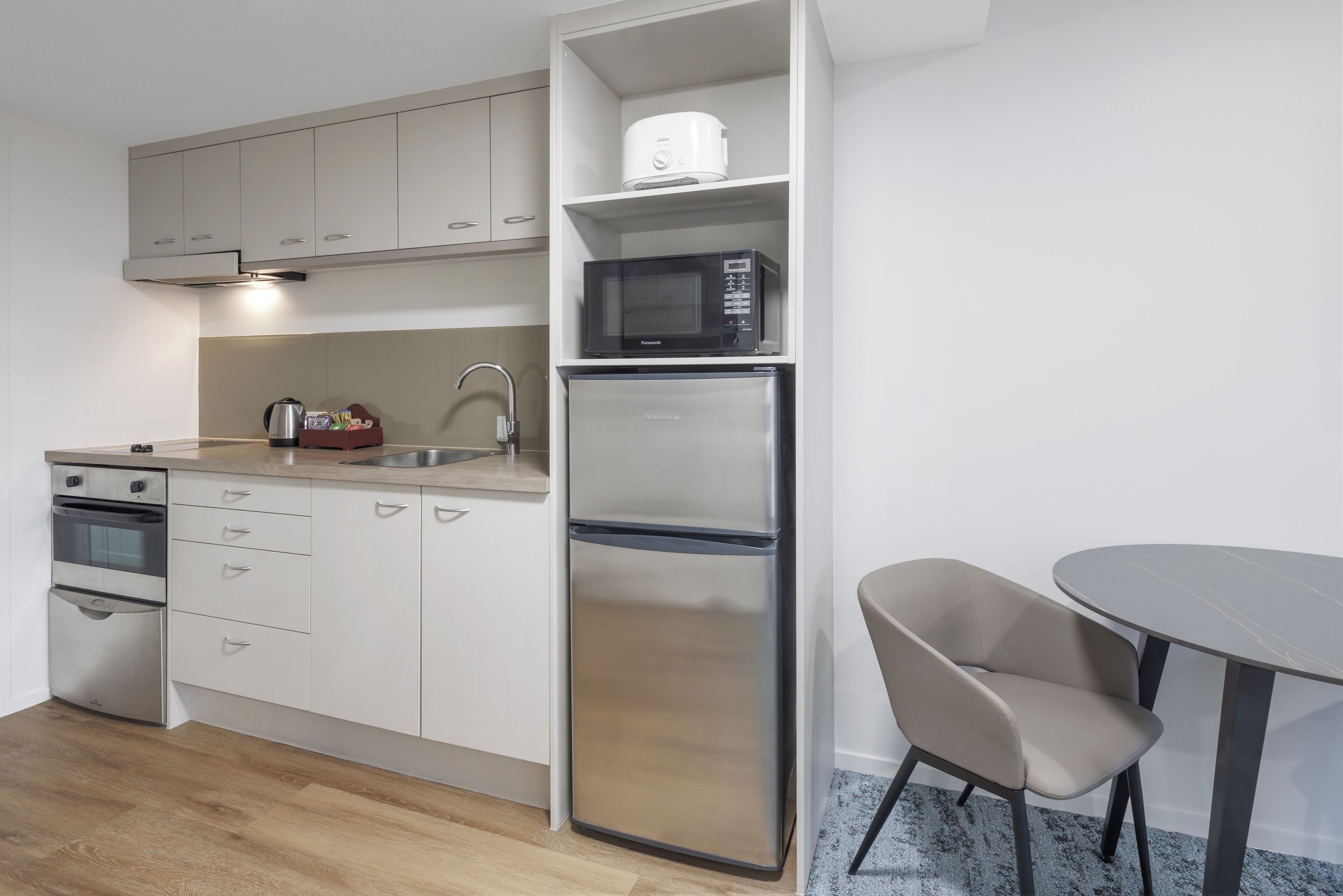 Een moderne keuken met roestvrijstalen apparatuur, een inbouwmagnetron en een eethoek met een ronde tafel en een stoel.
