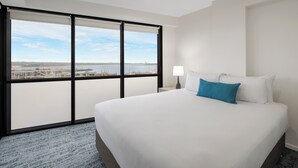 Hotelkamer met een groot bed, nachtkastje, lamp en uitzicht op het water en verre gebouwen.