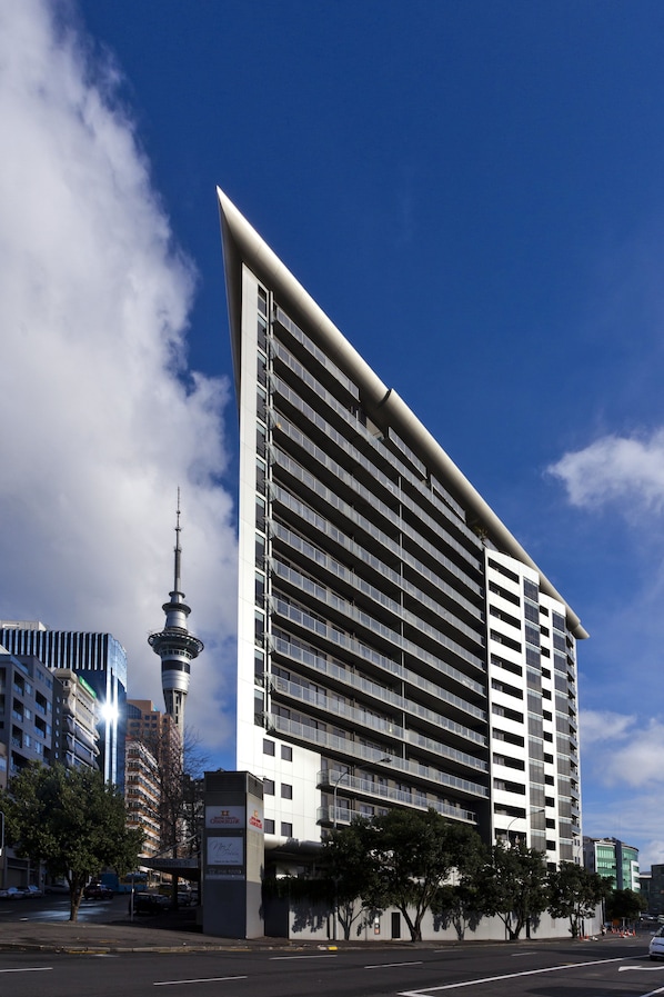 A modern high-rise hotel with a prominent tower structure, multiple balconies, and a clear sky. - The Chancellor on Hobson (Auckland)
