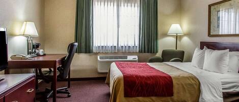 Una habitación de hotel con cama, escritorio con teléfono, silla, lámpara y ventana con cortinas.