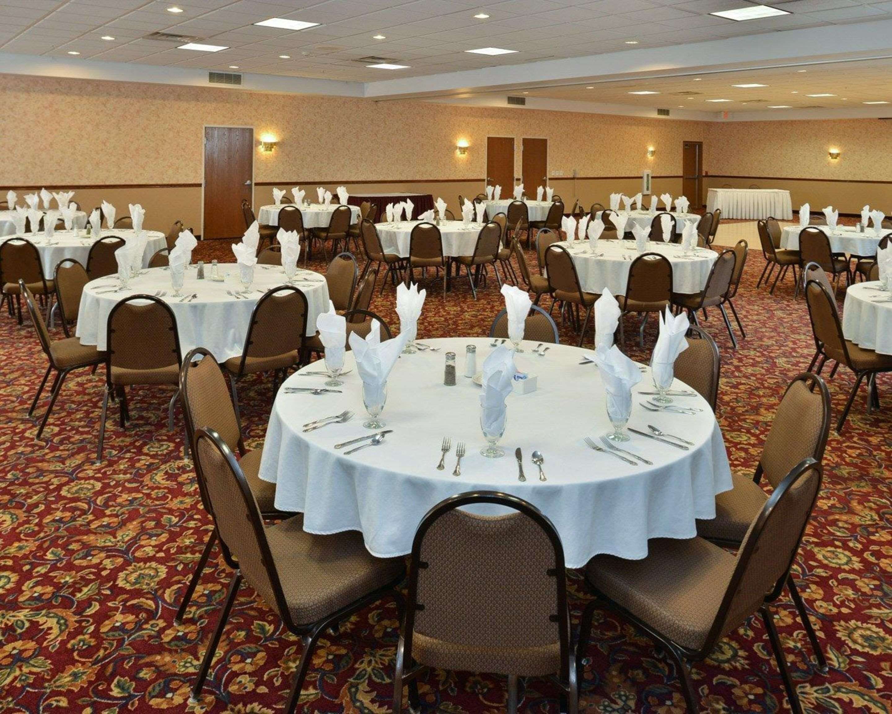 A banquet hall with round tables set for dining, each with white tablecloths and silverware.