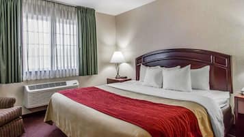 A hotel room with a large bed, a bedside table with a lamp, a chair, and a window with curtains.
