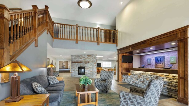 A spacious living area with a wooden staircase, a stone fireplace, and a reception desk. - Quality Inn & Suites Fort Madison near Hwy 61 (Fort Madison)