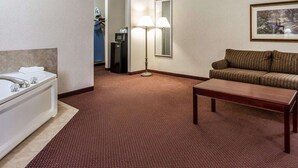 A hotel room with a bed, a desk, a sofa, a lamp, and a mirror. - Quality Inn & Suites Fort Madison near Hwy 61 (Fort Madison)