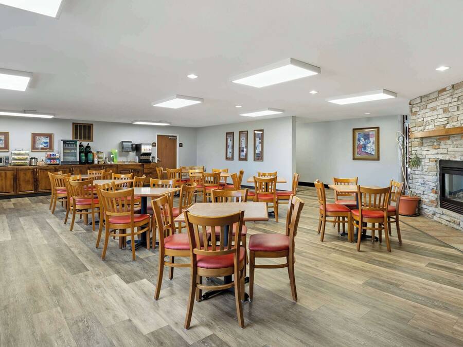 A spacious dining area with multiple wooden tables and chairs, a kitchen area with appliances, and a stone fireplace.