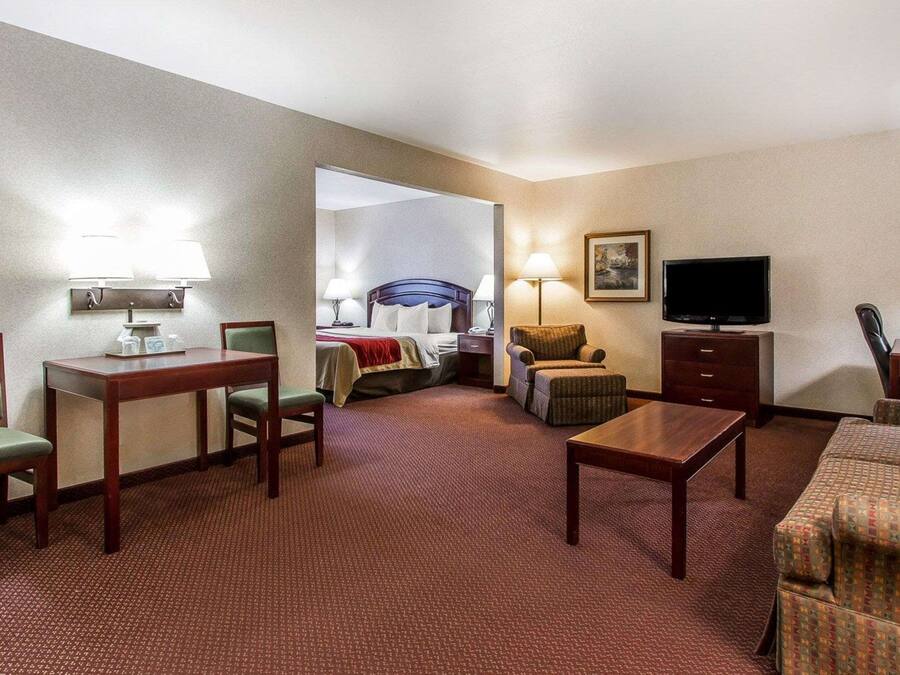 Quarto de hotel com cama, escrivaninha, poltrona, sofá, televisão e abajur.