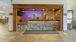 A reception area with a stone wall, wooden reception desk, and a sign that reads "Quality". - Quality Inn & Suites Fort Madison near Hwy 61 (Fort Madison)