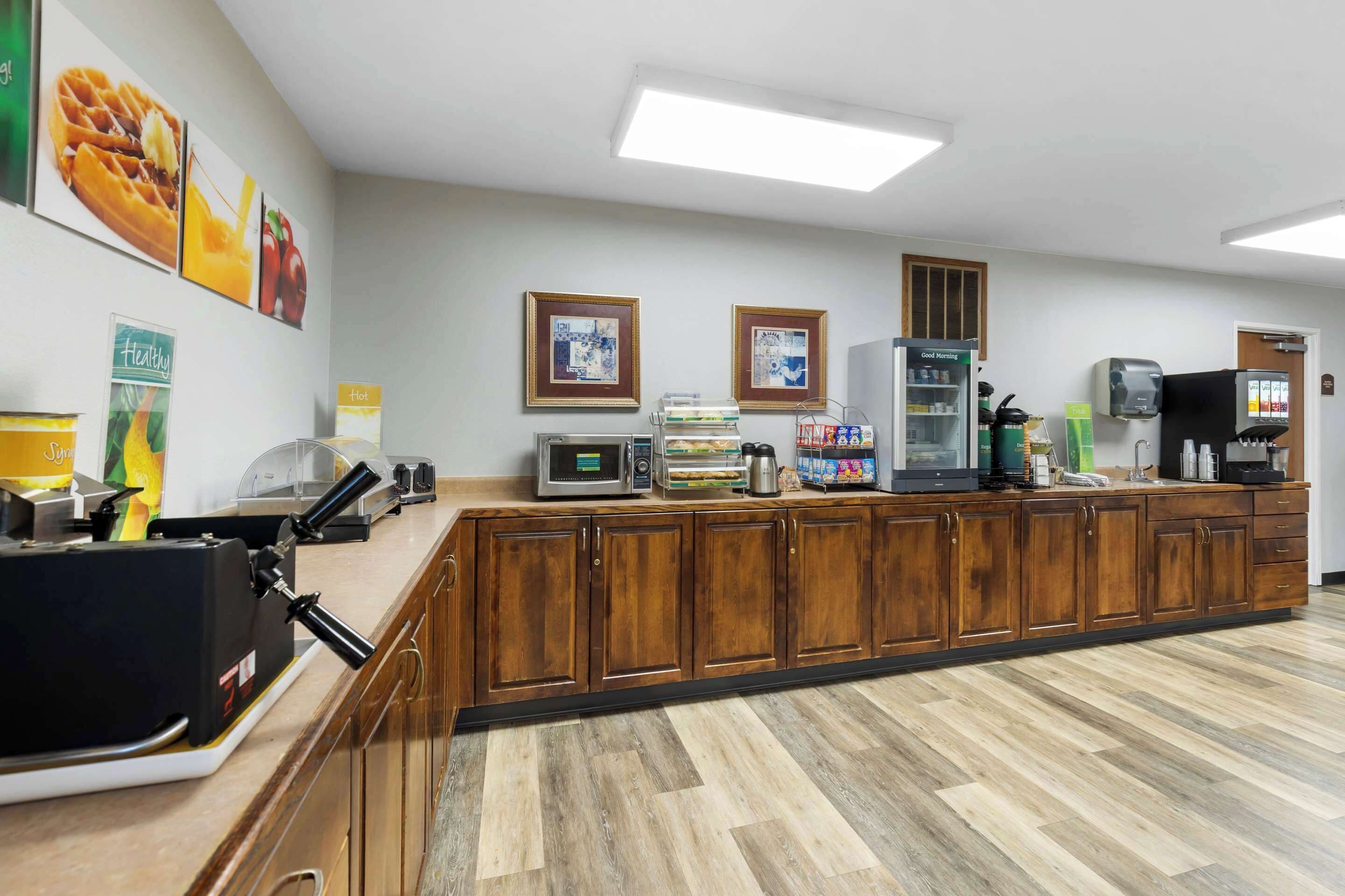 A kitchen area with wooden cabinets, a microwave, a coffee machine, and various food items on the counter.