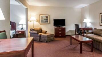 A hotel room with a flat-screen TV, a sofa, a chair, a small table, a desk, and a lamp.