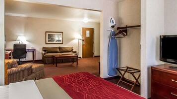 A hotel room with a bed, a desk with a chair, a sofa, a TV, and a wall-mounted ironing board.