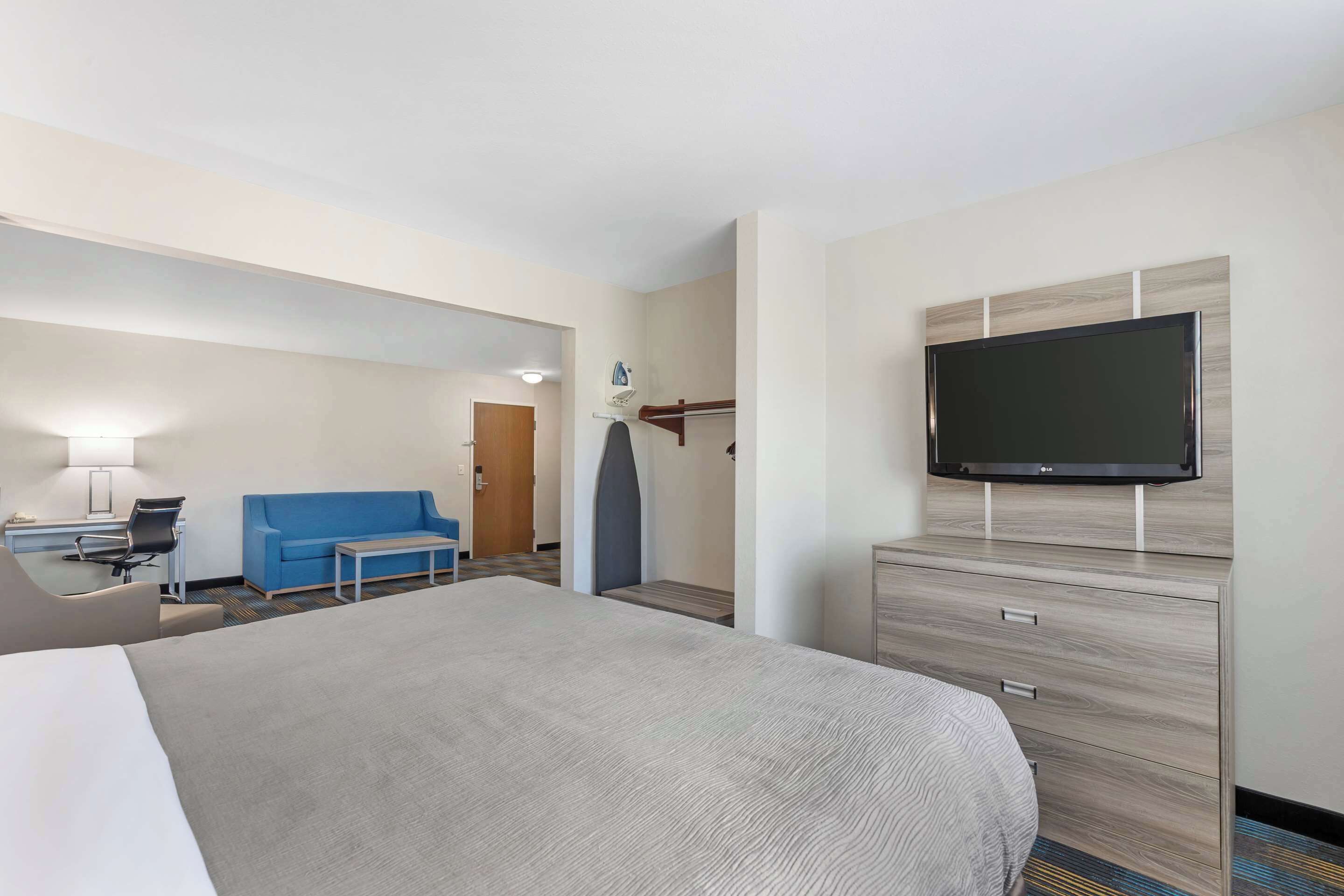 A hotel room with a large bed, a TV mounted on the wall, a desk with a chair, a blue sofa, and a small table.