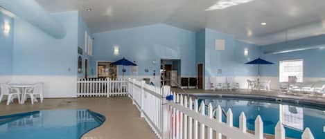 Une piscine intérieure entourée d’une clôture blanche en bois, avec des chaises longues et un plafond bleu.