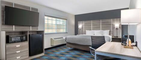 Une chambre d’hôtel équipée d’un lit, d’un bureau, d’un téléviseur à écran plat, d’un four à micro-ondes, d’un réfrigérateur, d’une fenêtre et d’une moquette à motifs.