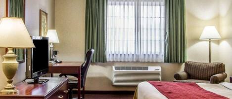 A hotel room with a bed, desk, chair, television, air conditioning unit, and two lamps.