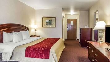A hotel room with a large bed, a dresser, a desk, a lamp, and a framed picture on the wall.