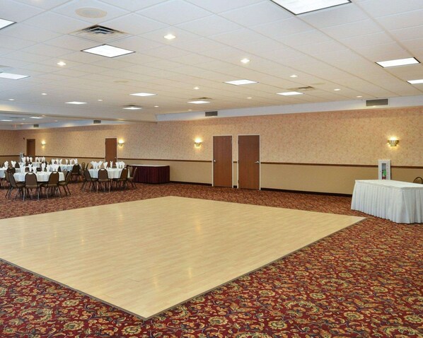 A large conference room with a wooden dance floor, carpeted walls, and tables set up for a meeting.