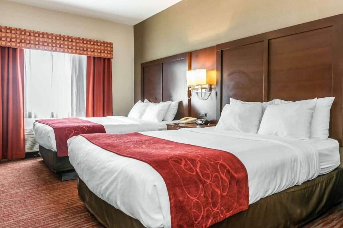 Habitación de hotel con dos camas, un ventanal con cortinas, una lámpara de noche y un teléfono en la mesita.