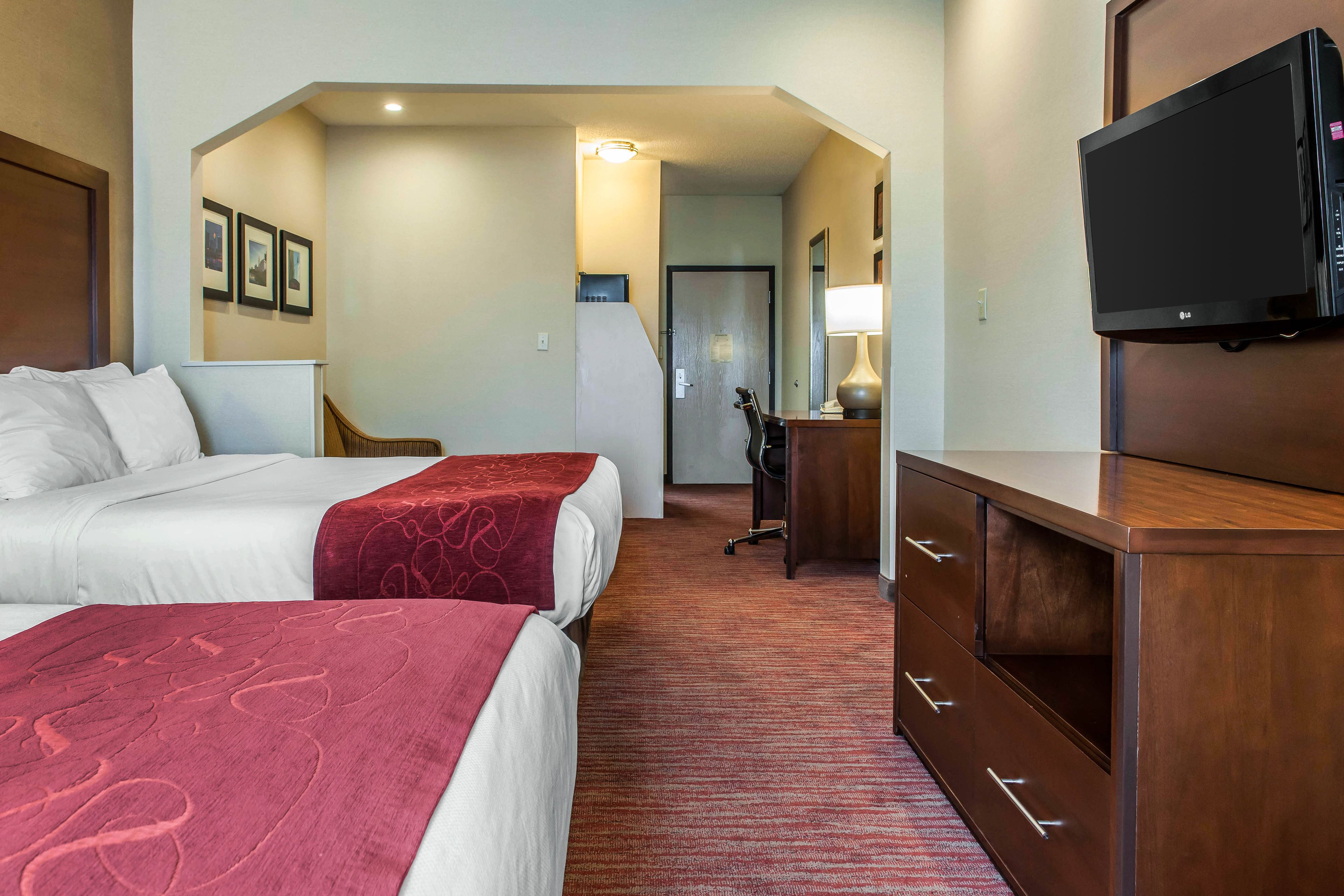 Une chambre d’hôtel avec deux lits, un bureau, une télévision et une porte donnant sur une autre pièce.