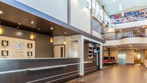 Un espace d’accueil d’hôtel au design moderne, comprenant un comptoir d’accueil, un escalier menant à l’étage supérieur et un espace repas avec des tables et des chaises.