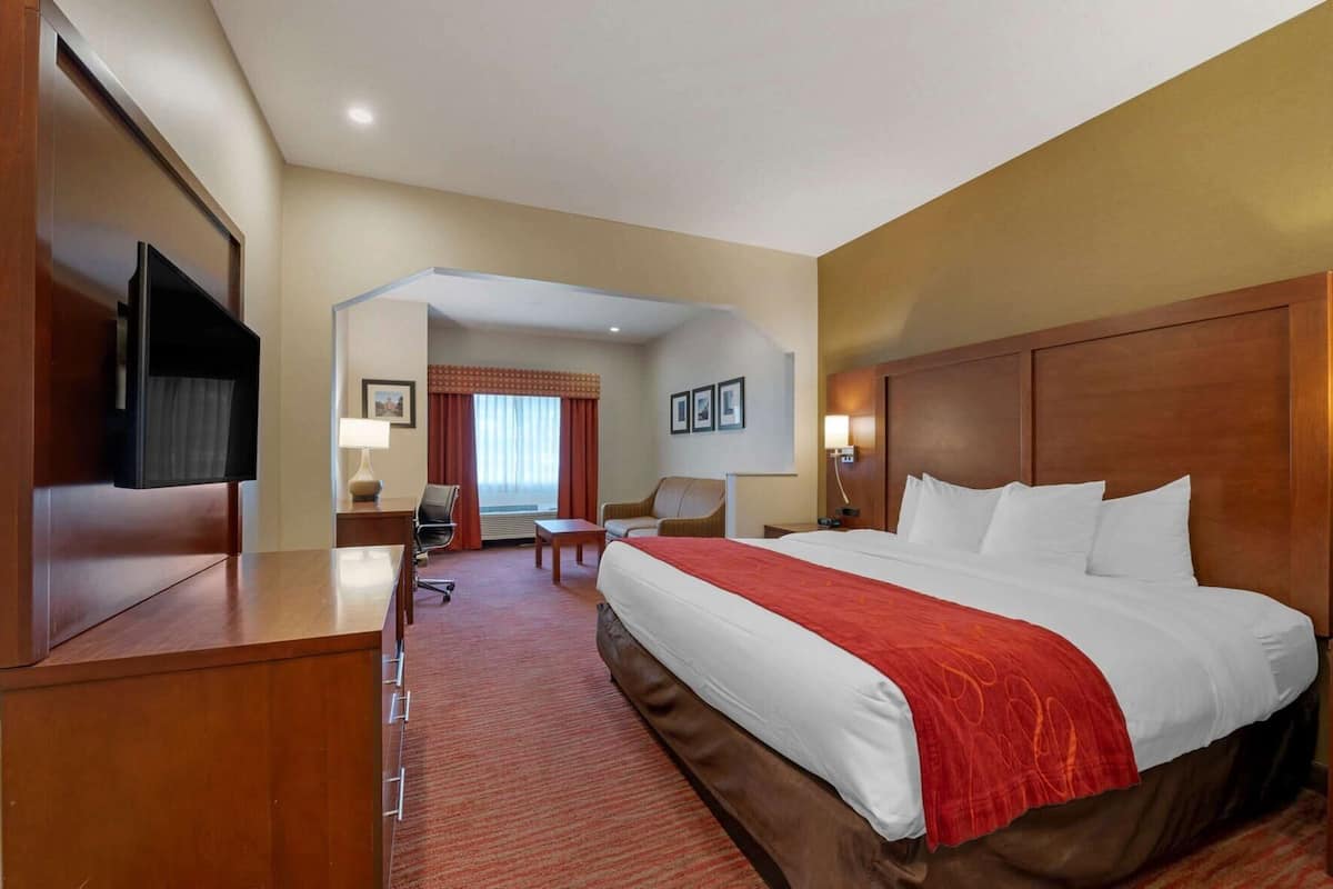 Habitación de hotel con una cama grande, un escritorio con televisor, una silla, una mesita y una ventana con cortinas.