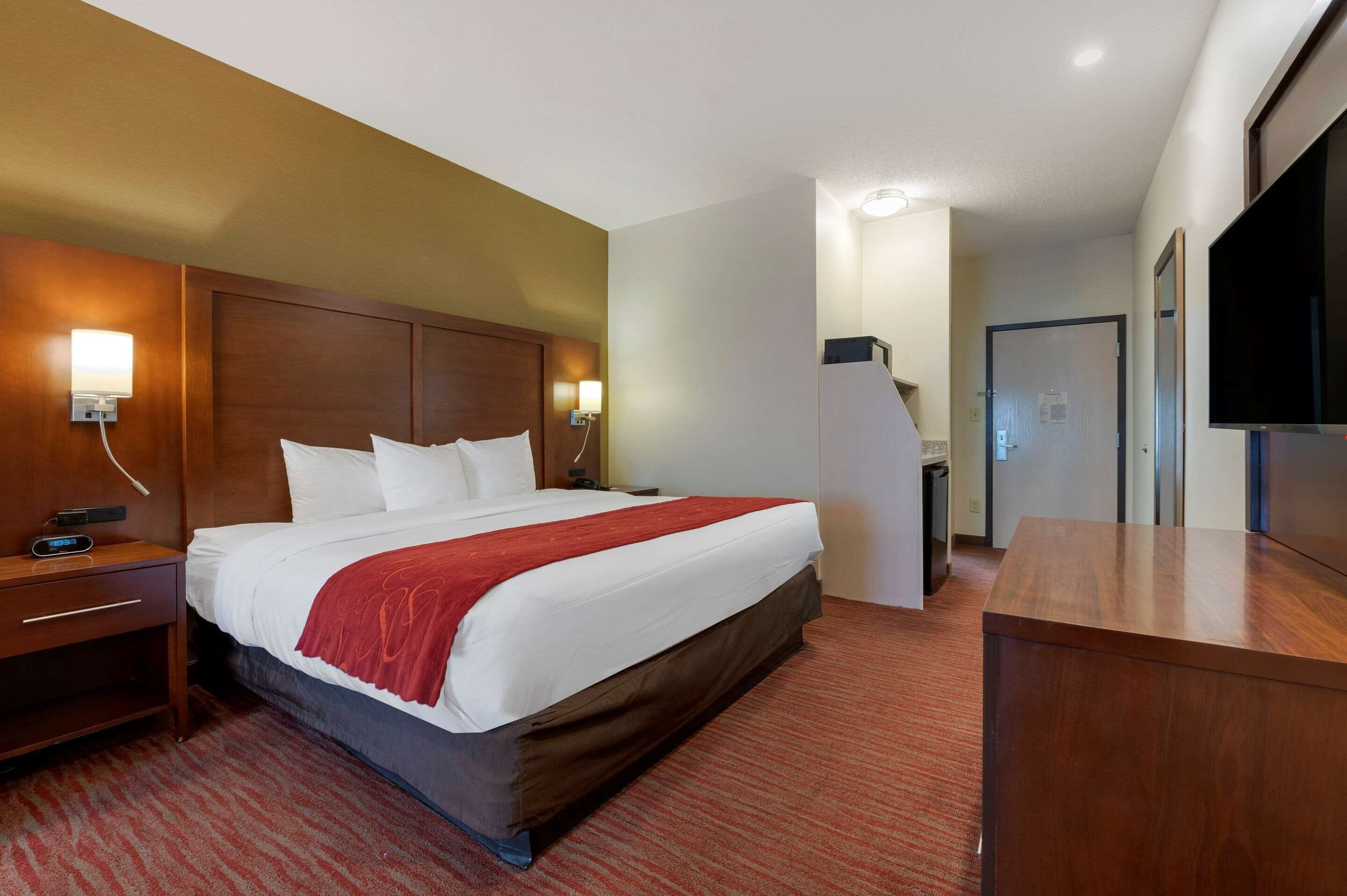 A hotel room with a large bed, wooden headboard, bedside lamps, a desk, and a flat-screen TV.