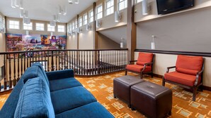 Un hall d’hôtel avec un canapé bleu, des fauteuils rouges, une moquette à motifs, un escalier et un grand téléviseur fixé au mur.