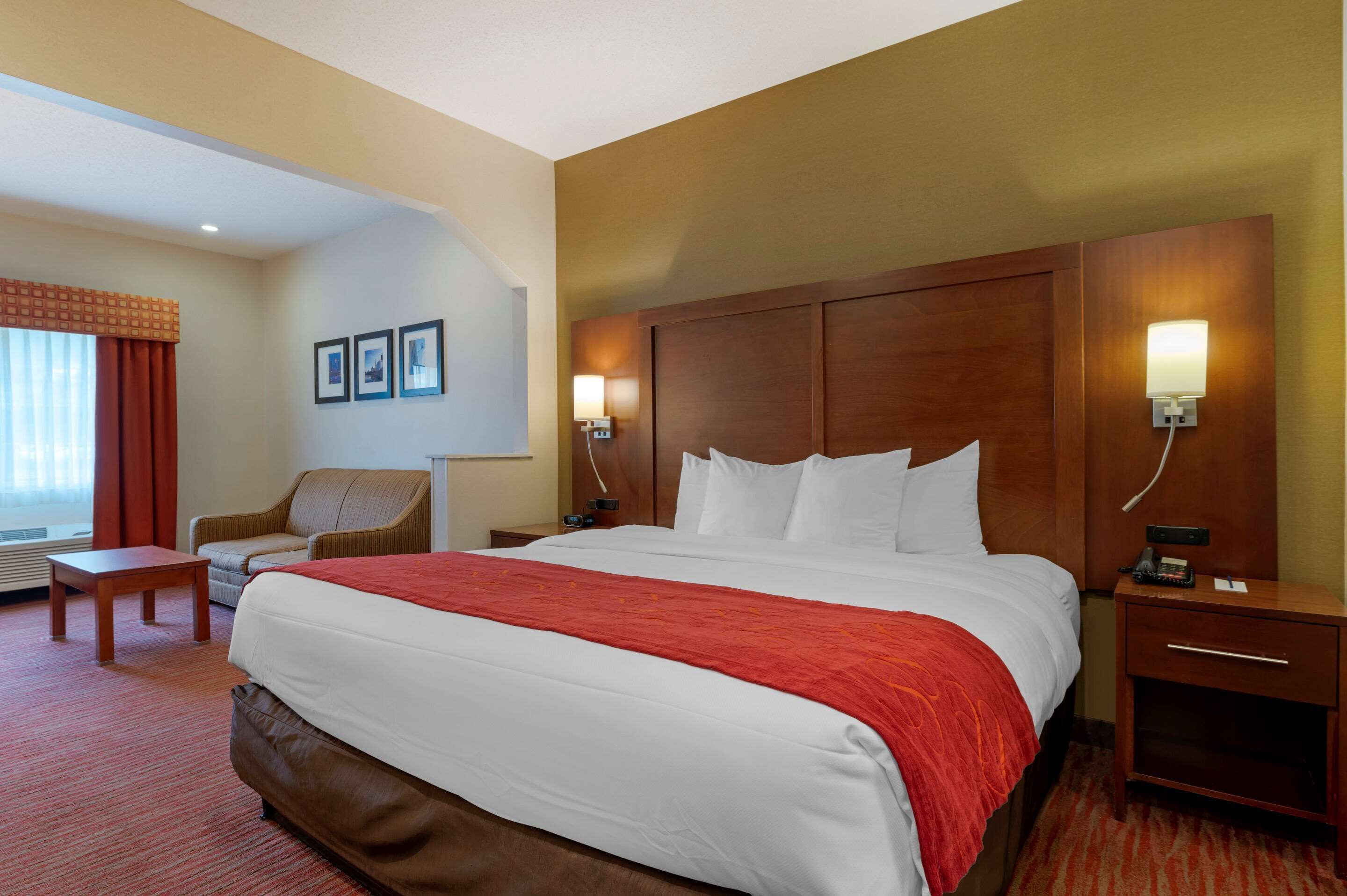 A hotel room with a large bed, a wooden nightstand, a chair, and a desk.