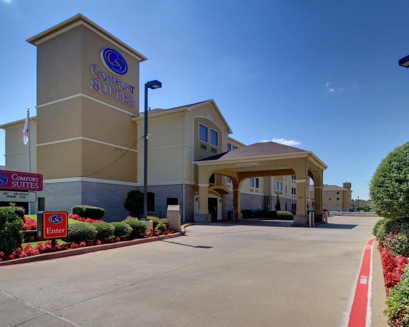 Um hotel Comfort Suites com entrada acessível, área de estacionamento coberta e placa indicando as comodidades do hotel.