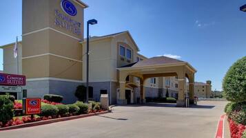 Um hotel Comfort Suites com entrada acessível, área de estacionamento coberta e placa indicando as comodidades do hotel.