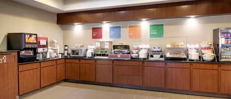 A self-service breakfast area with coffee machines, food dispensers, and a refrigerator.