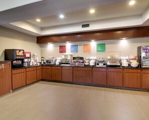 Ein Bereich für das Frühstück mit Selbstbedienung, inklusive Kaffeeautomaten, Speisenausgabegeräten und einem Kühlschrank.