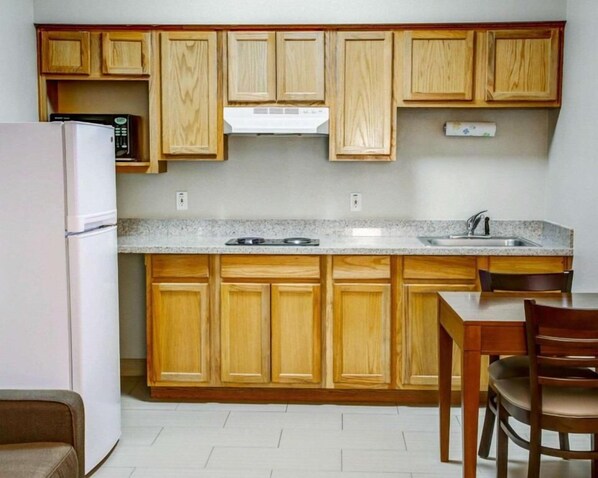 A compact kitchen with wooden cabinets, a built-in microwave, a stove, and a sink. - Comfort Suites Tyler South (Tyler)