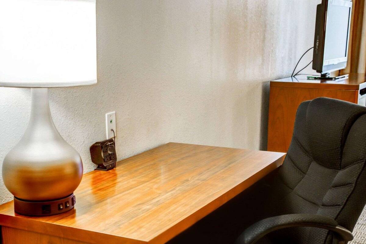 A wooden desk with a lamp, a power outlet, and a black office chair.