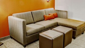 A sectional sofa with a footstool and ottoman, a patterned rug, and a wall with framed pictures.