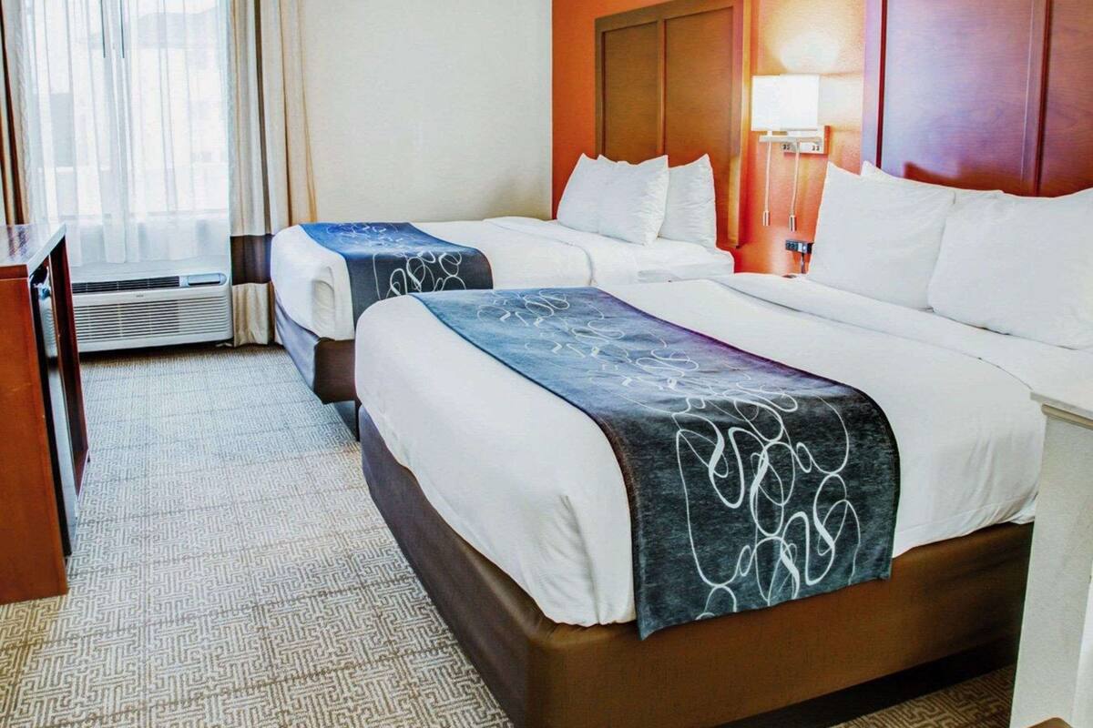 A hotel room with two beds, a desk, and a window with curtains.