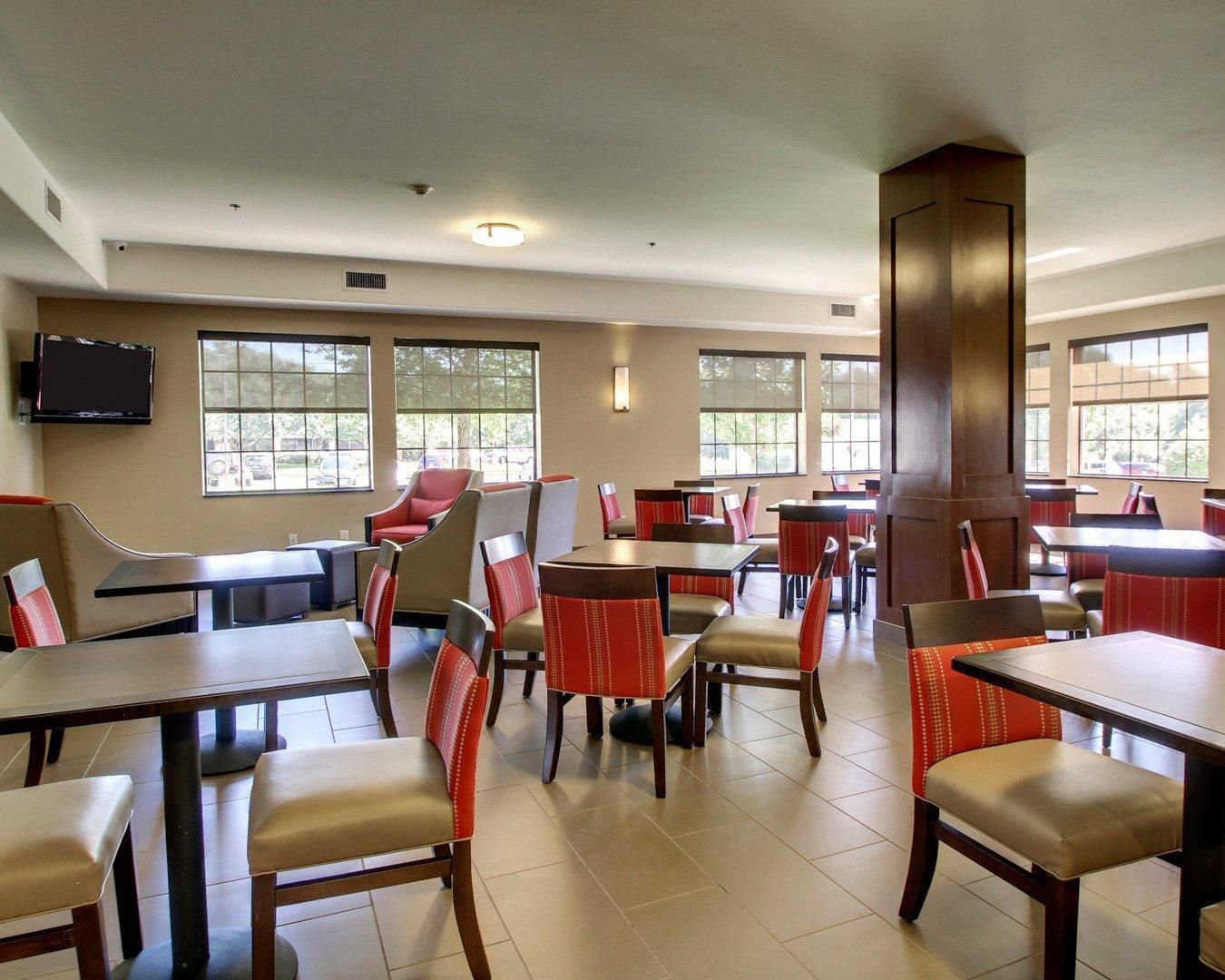 Un ristorante con diversi tavoli e sedie, una televisione a schermo piatto montata a parete e ampie finestre che lasciano entrare luce naturale.