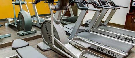 A hotel fitness center with treadmills, ellipticals, and a bench.